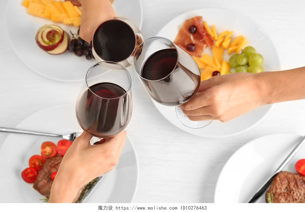 白色桌子上摆放着美食与正在碰杯的葡萄酒杯